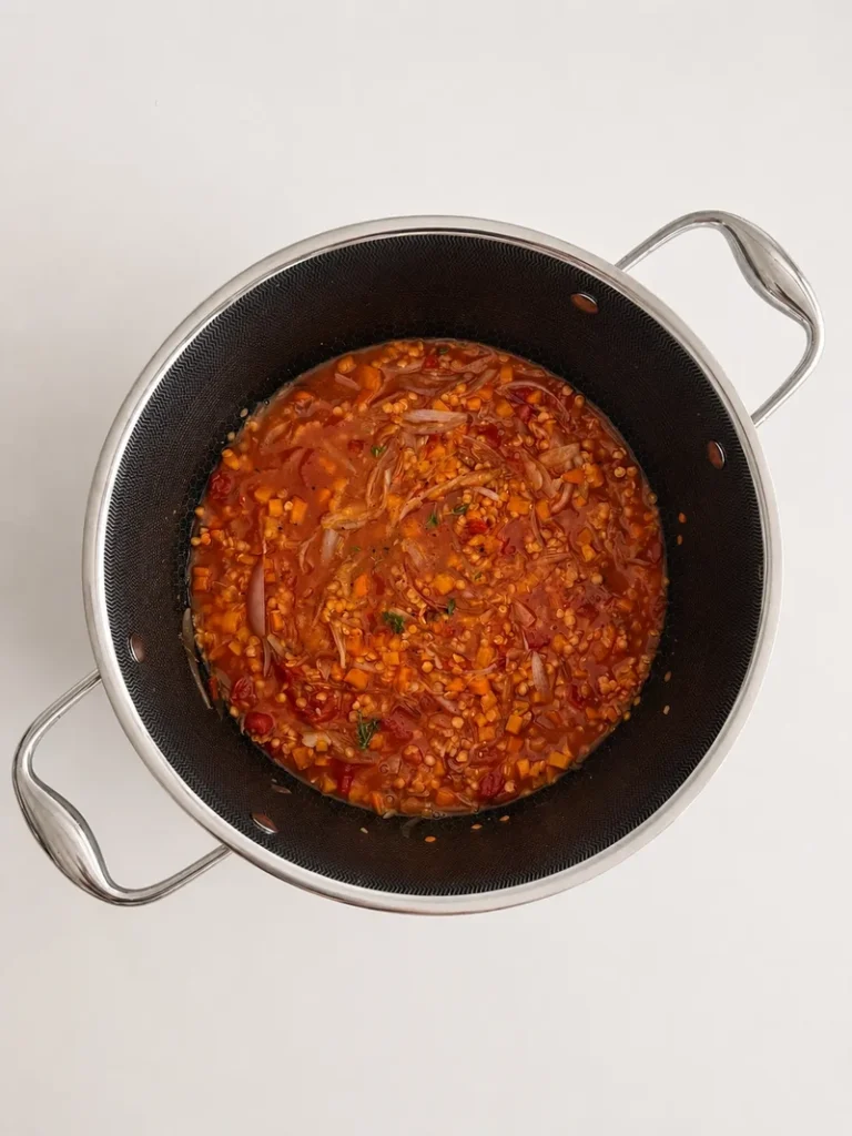 French onion soup with lentils simmering in a pot with caramelized onions, red lentils, tomato and carrots.