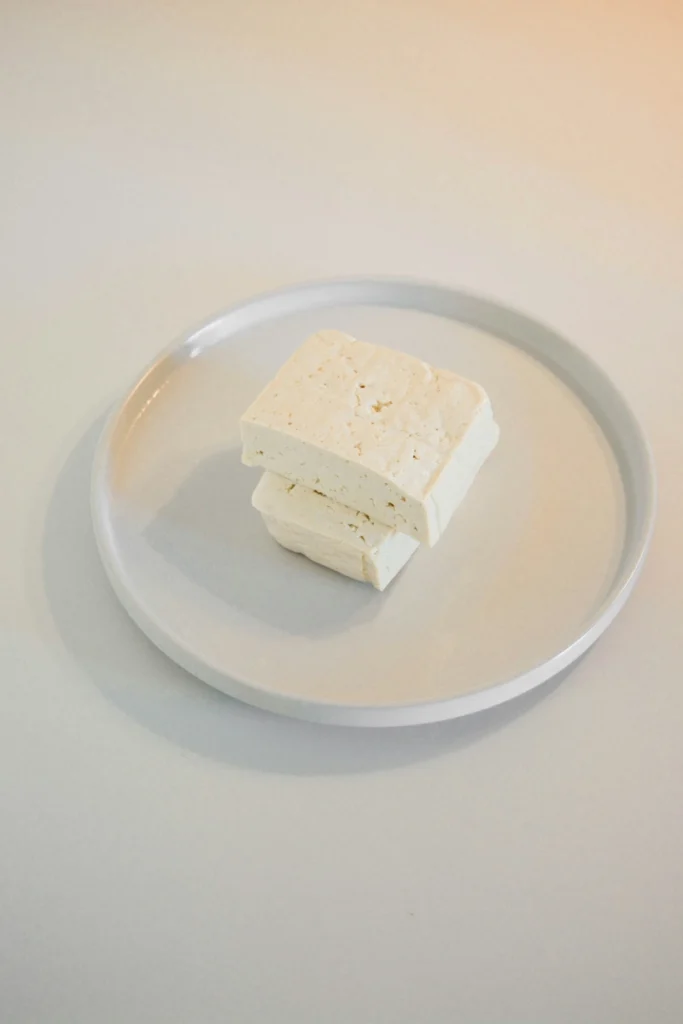 Stacked pieces of firm tofu on a white plate, photographed in soft natural light.