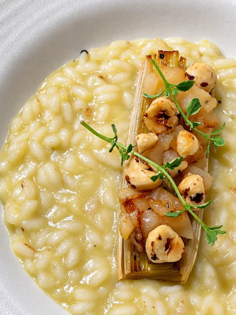 Creamy vegan risotto topped with roasted leek, toasted hazelnuts and fresh microgreens.