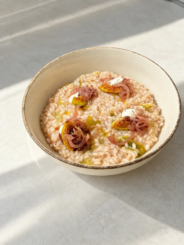Creamy vegan fig risotto served in a light ceramic bowl, topped with fresh figs, pickled red onions and small dollops of vegan cheese.