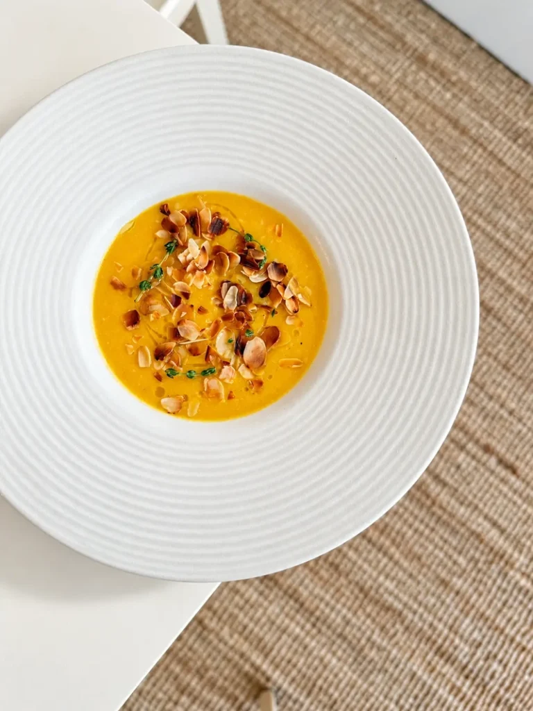 Overhead view of lemon carrot cauliflower soup topped with toasted almonds, fresh thyme and a drizzle of olive oil.