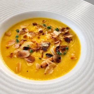 Lemon carrot cauliflower soup topped with toasted almonds, fresh thyme and olive oil, served in a wide white bowl.