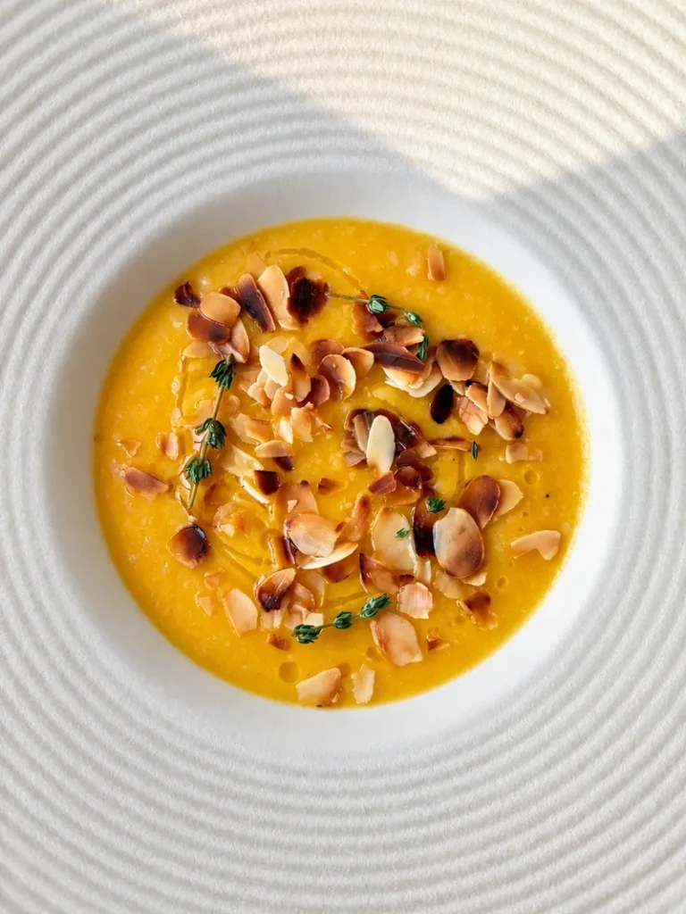 Creamy lemon carrot cauliflower soup with toasted almonds and thyme, photographed close up in a white ceramic bowl.