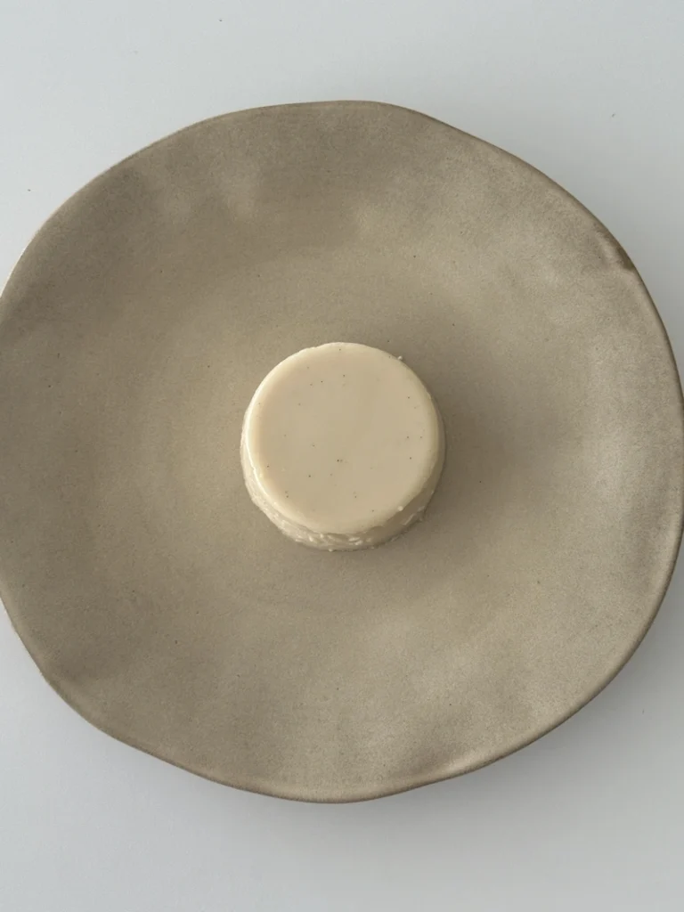 Unmolded vegan panna cotta served on a ceramic plate, showing its smooth white surface and delicate set texture.