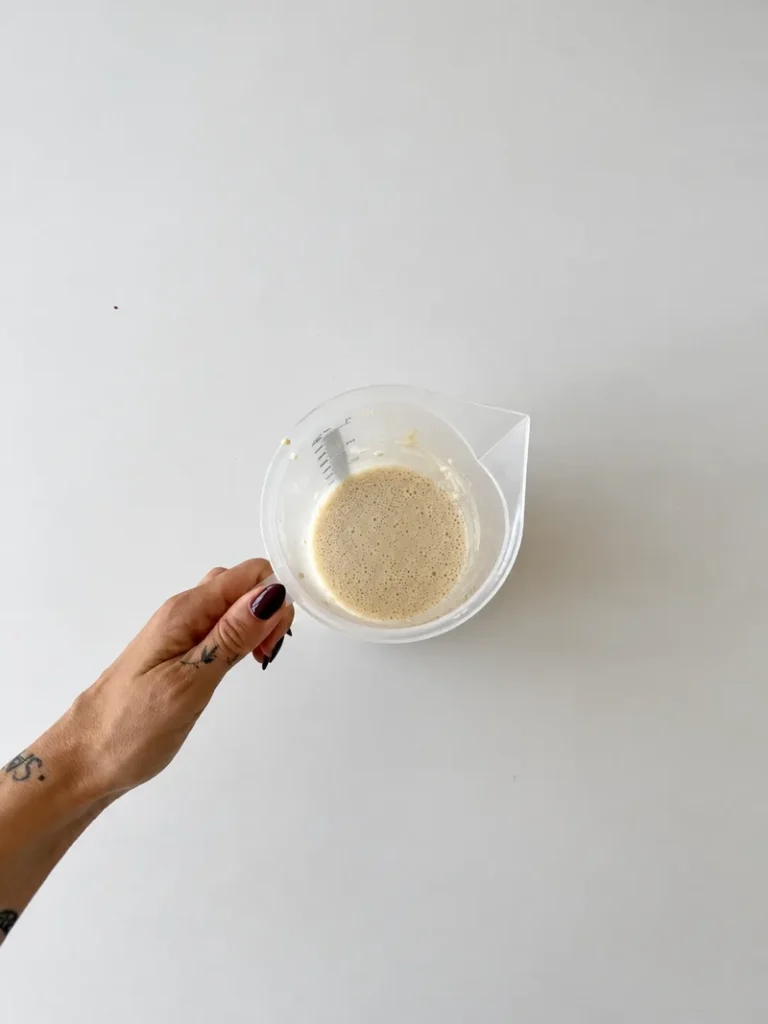 Vegan panna cotta mixture in a measuring jug, held by hand over a white surface before being poured into the molds.