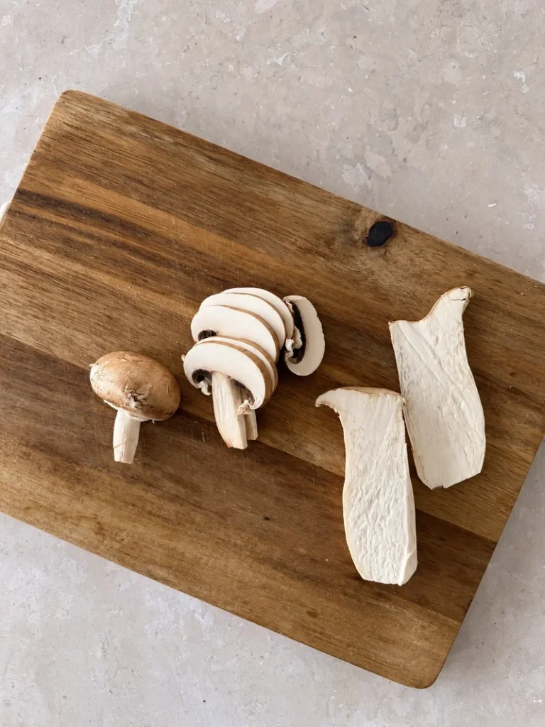 Fresh mushrooms sliced in different sizes on a wooden cutting board, ready to cook for vegan mushroom risotto.