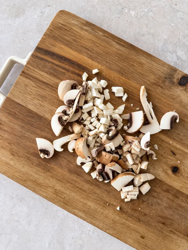 Mixed mushrooms chopped into small irregular pieces on a wooden cutting board for vegan mushroom risotto.