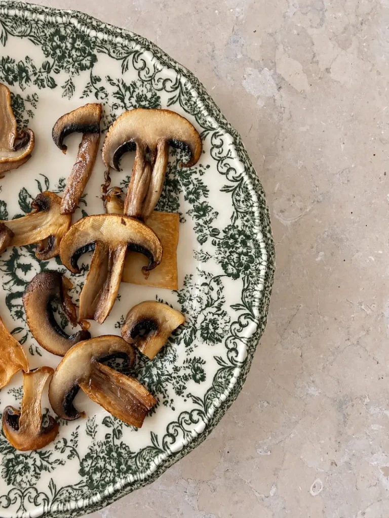 Golden sautéed mushroom slices arranged on a vintage green and cream plate for vegan mushroom risotto.