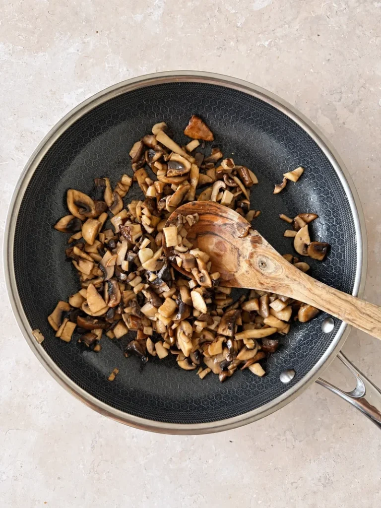 Chopped mixed mushrooms sautéing in a pan with a wooden spoon for vegan mushroom risotto.