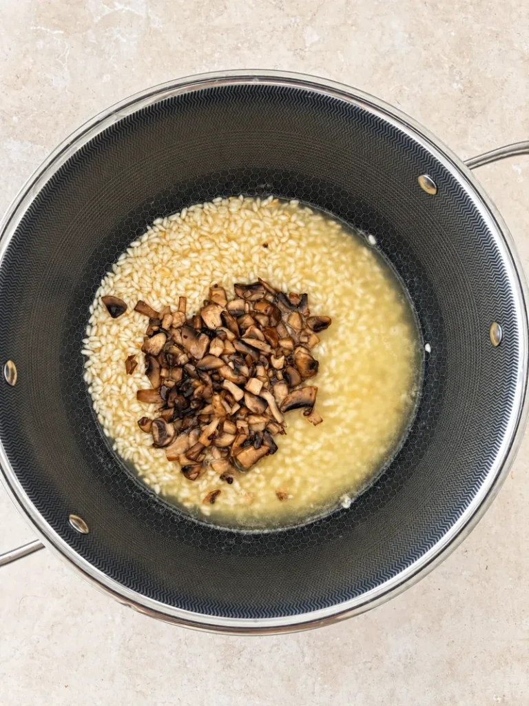Vegan mushroom risotto cooking in a pan with sautéed mixed mushrooms added to the rice and hot broth.