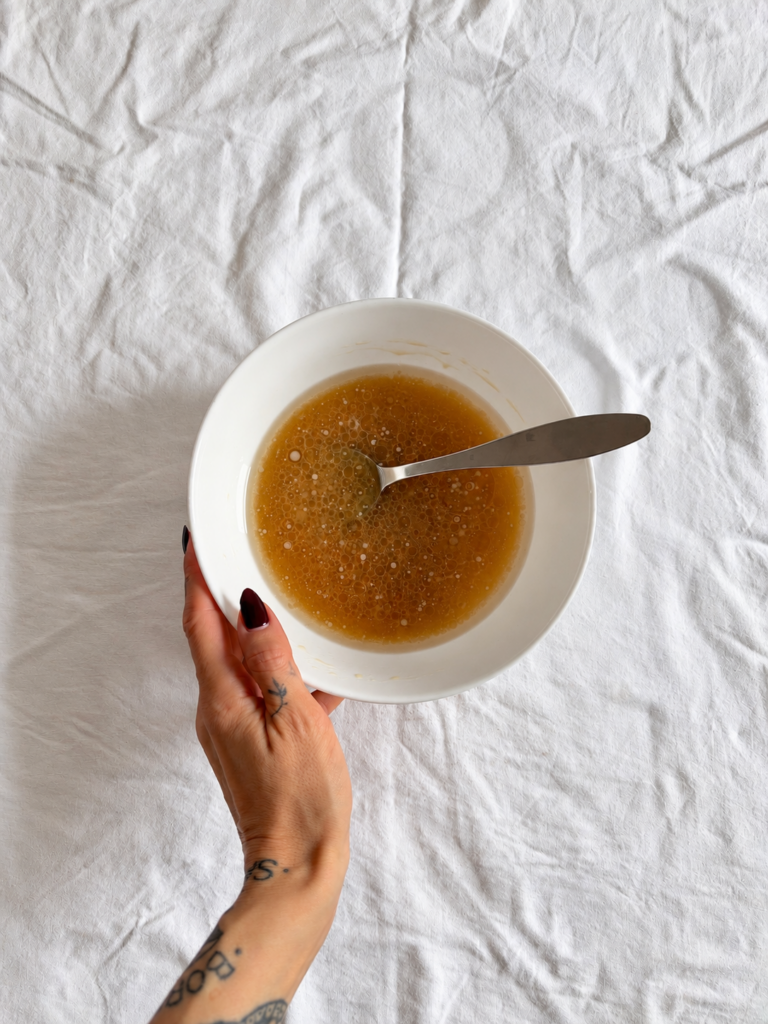Mixed wet ingredients for vegan chocolate pear cake in a white bowl, held by hand during the recipe process.