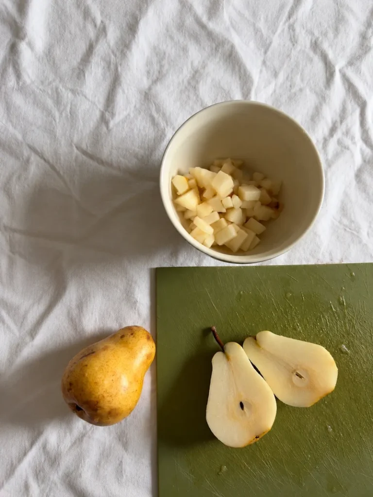 Pears being prepared for vegan chocolate pear cake, with diced pear in a bowl and halved pears on a cutting board.