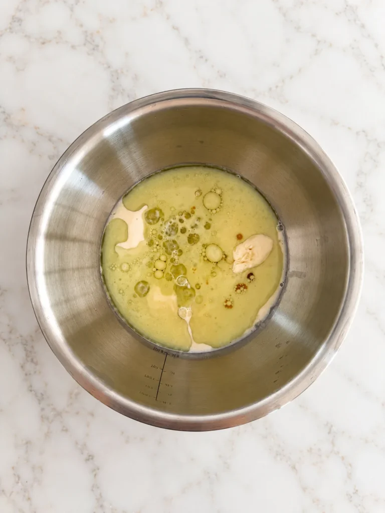Stainless steel mixing bowl containing plant-based milk, yogurt, oil and other wet ingredients for a healthy vegan gluten-free apple bread recipe.