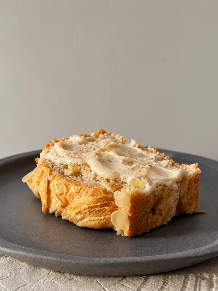 Slice of healthy apple bread topped with cashew cream on a dark plate.
