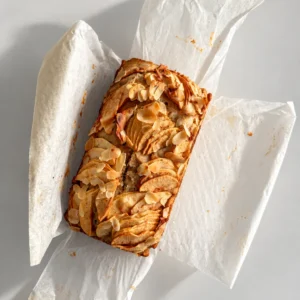 Top view of baked healthy apple bread with sliced apples and flaked almonds on parchment paper.