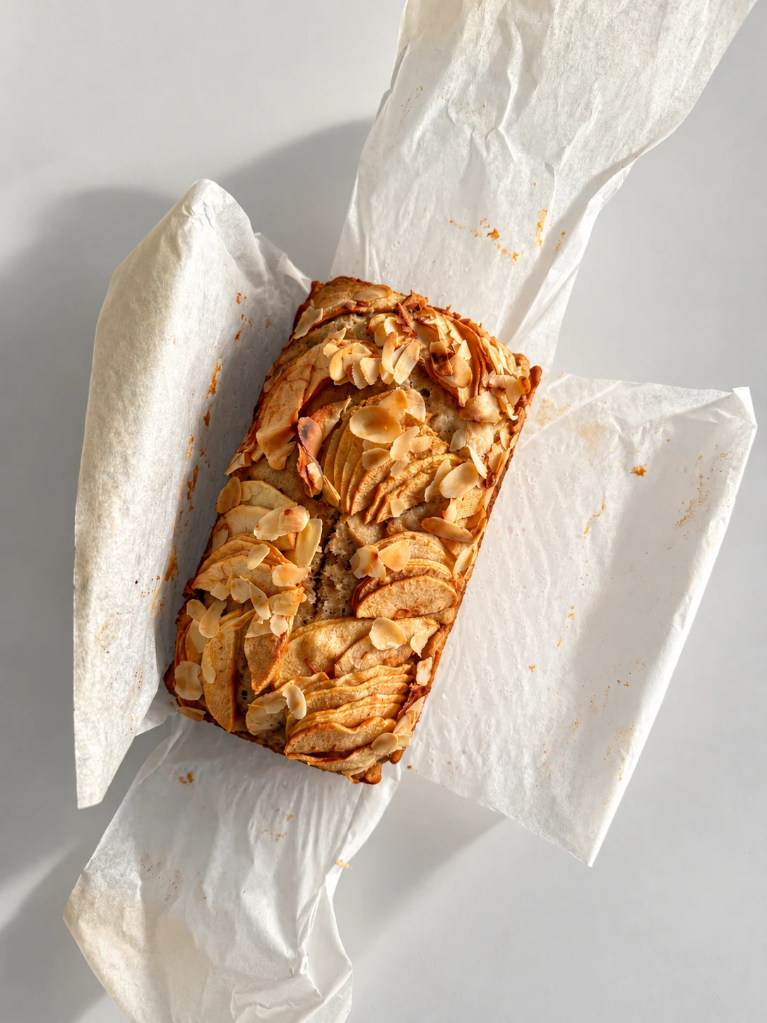 Top view of baked healthy apple bread with sliced apples and flaked almonds on parchment paper.