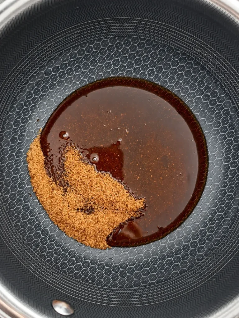 Coconut sugar and syrup in a saucepan at the beginning of the caramel sauce, shown from above on a patterned non-stick pan.
