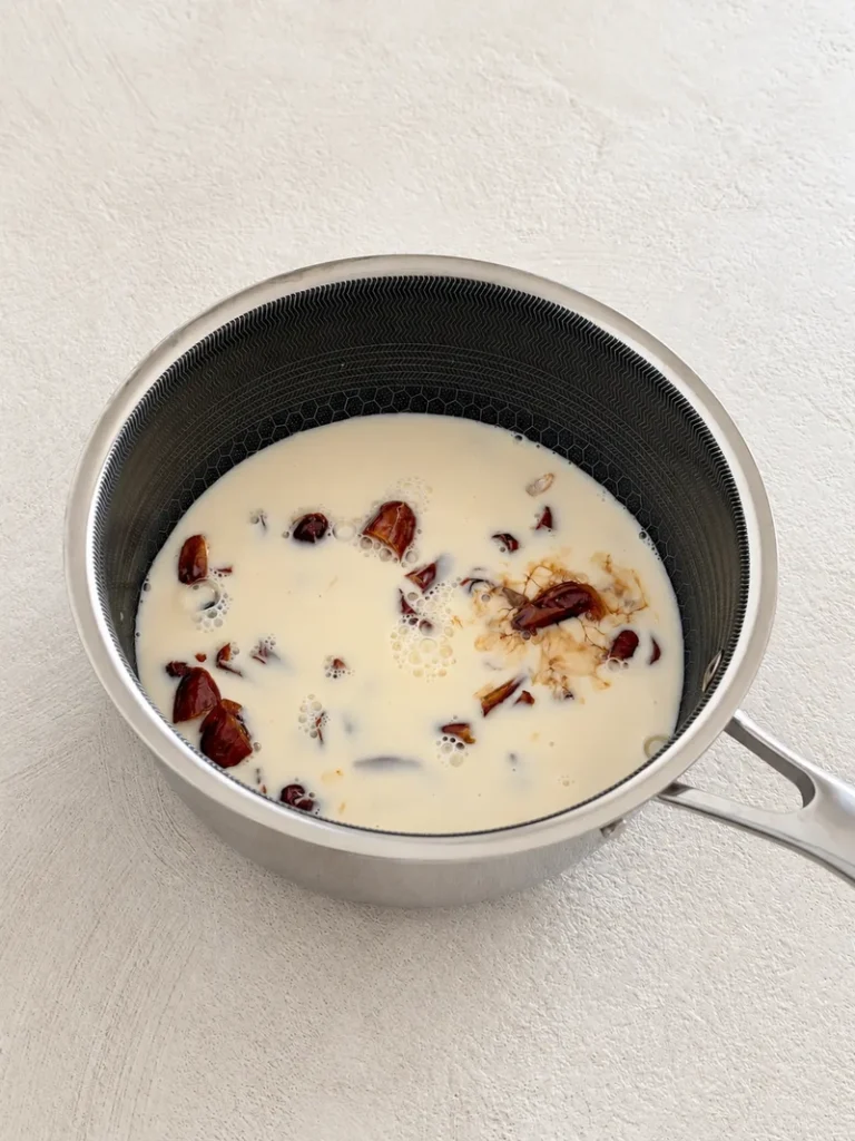 Medjool dates simmering in unsweetened soy milk in a saucepan, the first step in preparing vegan gluten free sticky toffee pudding.