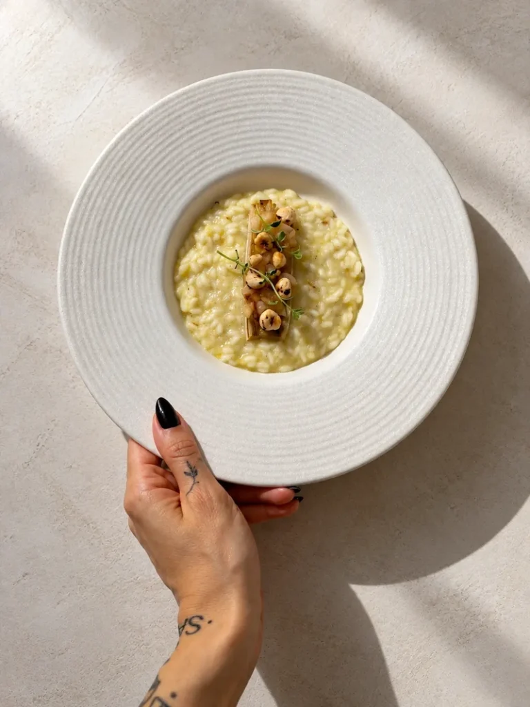 Vegan leek risotto with pear and hazelnuts served in a white bowl, topped with roasted leek, sautéed pear, hazelnuts and lemon thyme.