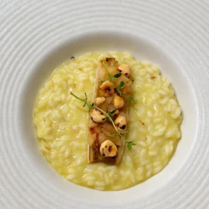 Vegan leek risotto with sautéed pear, toasted hazelnuts, roasted leek and fresh thyme, served in a wide white bowl.