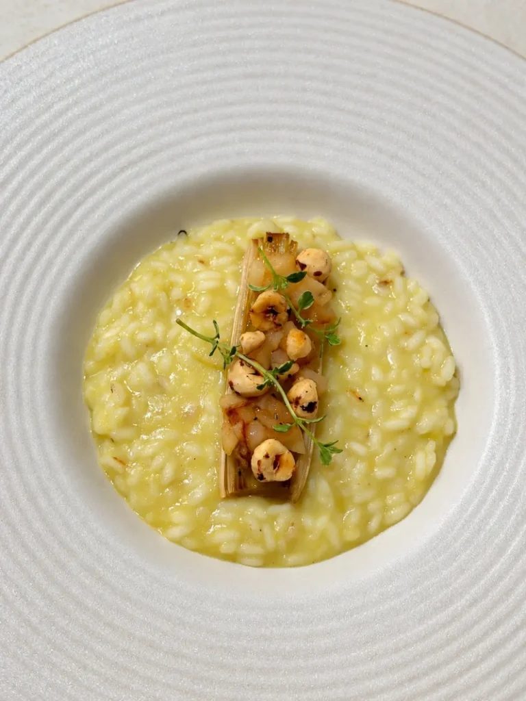 Vegan leek risotto with sautéed pear, toasted hazelnuts, roasted leek and fresh thyme, served in a wide white bowl.