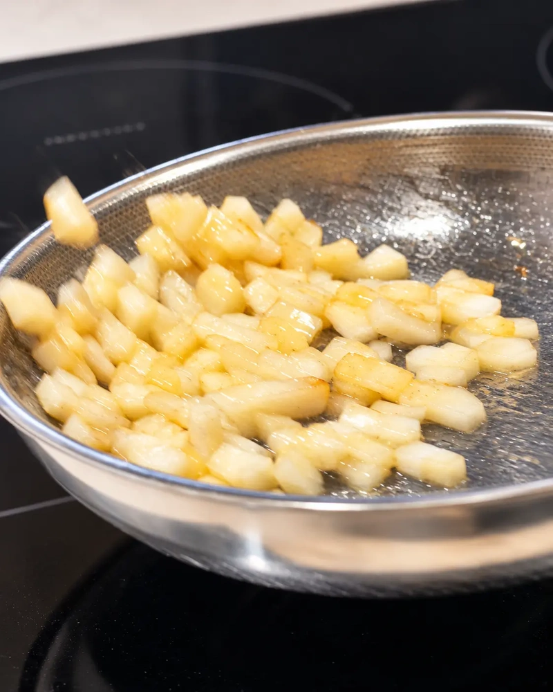Diced pear being tossed in a hot pan with butter and oil, lightly golden at the edges, for vegan leek risotto.