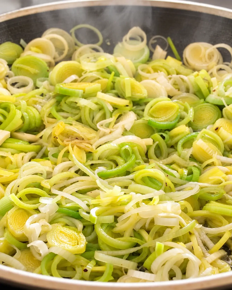 Sliced leeks cooking in a pan, photographed up close with steam rising, for vegan leek risotto.